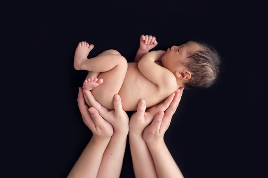 newborn baby photo lying in parents' hands