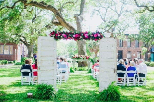 Beautiful outdoor wedding with white chairs and a floral arch.