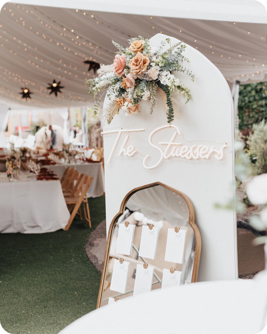 Peach roses spilling off a personalized welcome arch, a vintage gilt mirror standing in for the seating chart, and starburst pendants strung beneath a draped tent ceiling