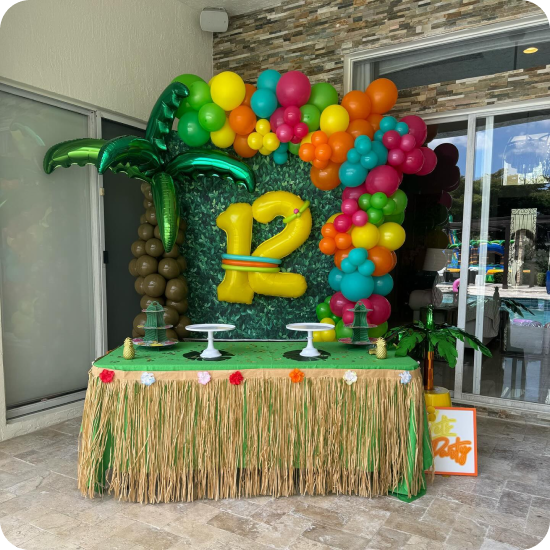 The balloon arch pulls every shade of summer into one frame — pinks, oranges, teals, and greens — and lets that giant yellow "12" do the talking.