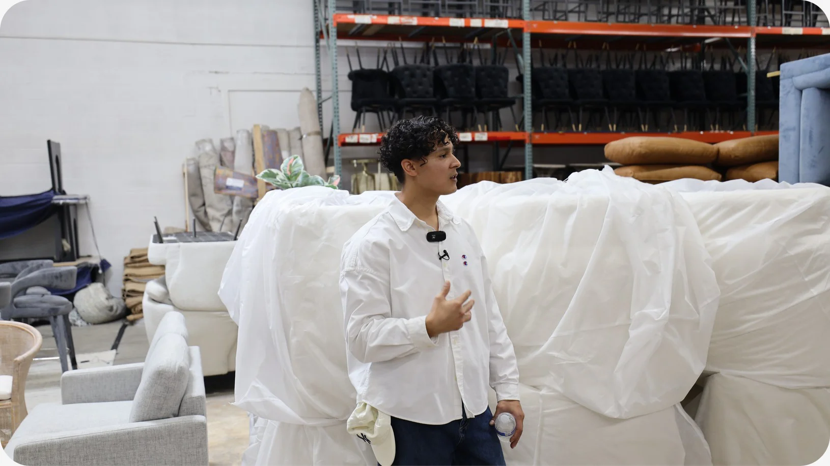 Gustavo Ortega, operations lead at Staging Design DC, talks beside sofas under white covers, with black dining chairs racked on the shelving behind him